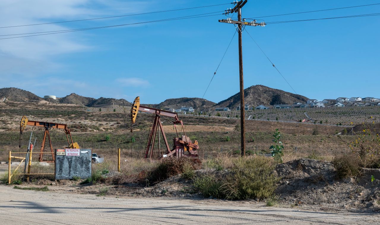 Two fenced oil pumpjacks in dry hills below a new hillside housing tract, the Kern County mix of energy and residential work