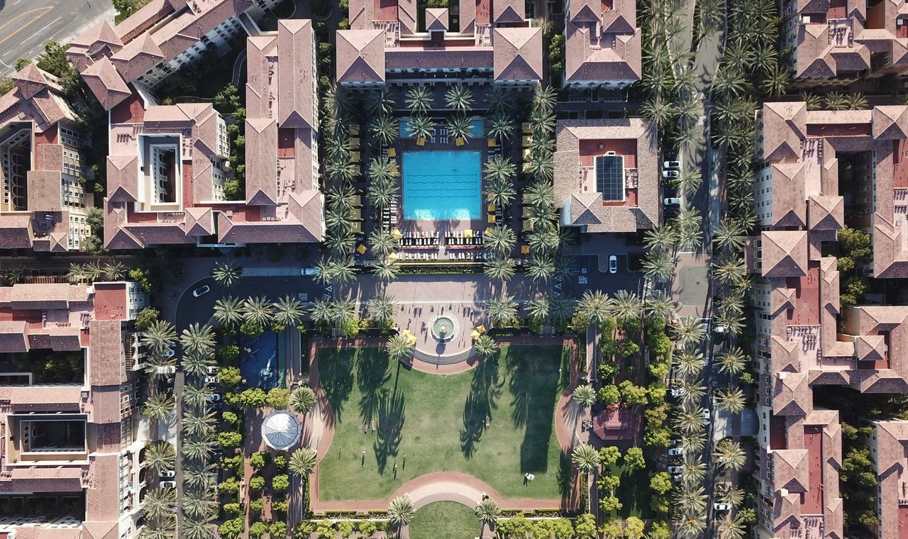 Overhead view of an Irvine apartment village with tiled roofs, a central pool and palm-lined paseos, the master-planned residential work FinTruction costs by phase