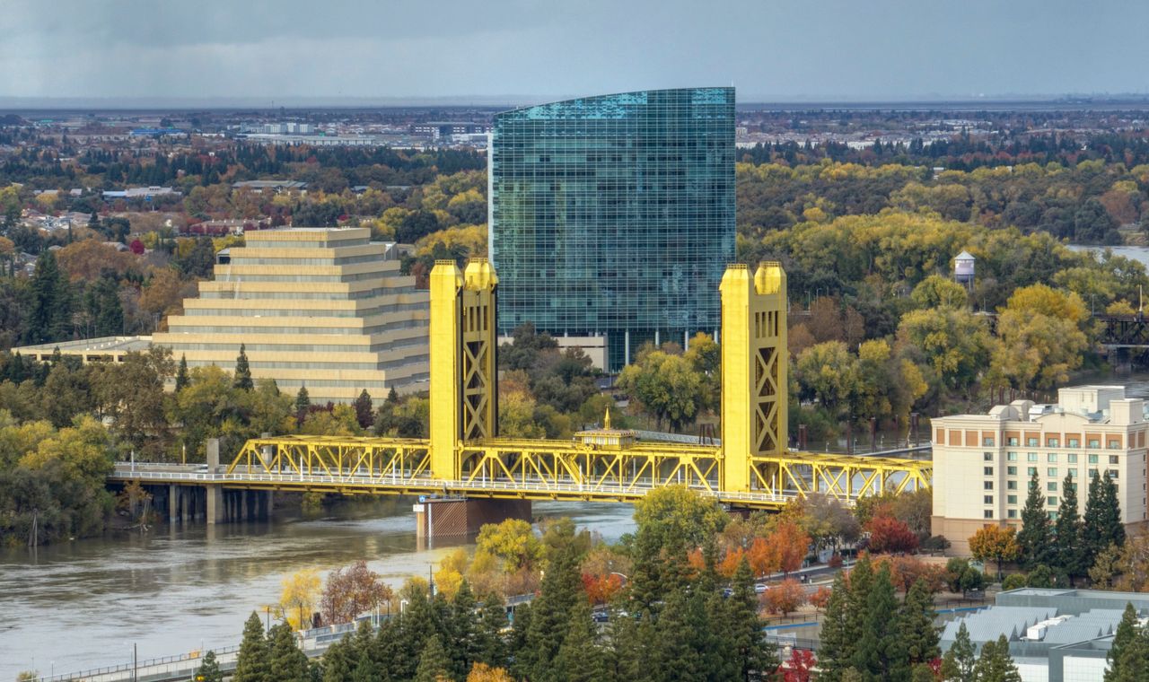 Tower Bridge in its yellow paint crossing the Sacramento River in autumn with West Sacramento offices beyond, where FinTruction keeps contractor books