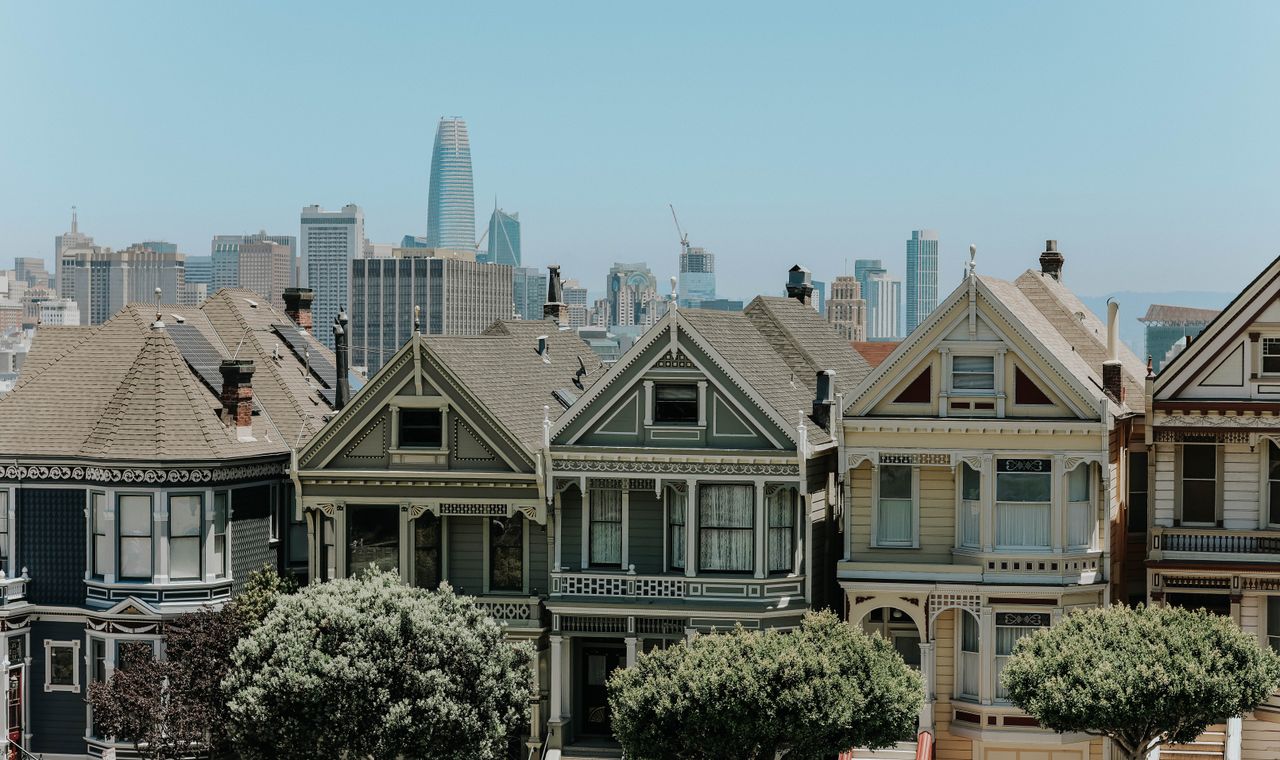 A row of painted Victorian houses on a hill with the downtown San Francisco high-rise skyline behind them, the mixed building stock FinTruction supports with contractor bookkeeping