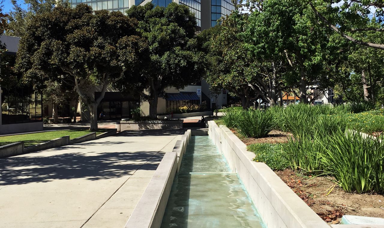 Glass office tower above a landscaped plaza and water channel in central Santa Ana, near the Orange County civic core