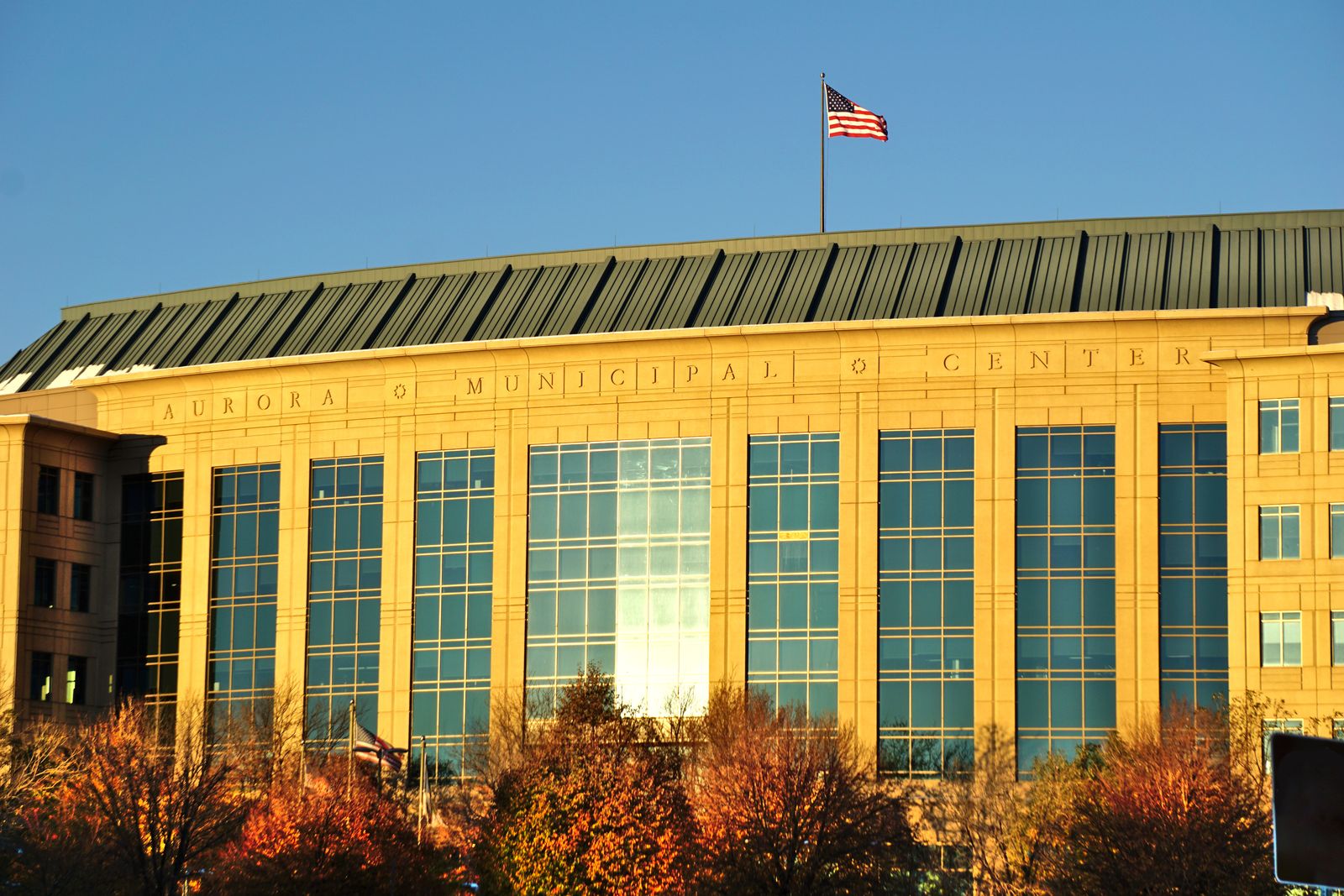 The Aurora Municipal Center in Colorado, its name carved above tall windows beneath a US flag in late afternoon light