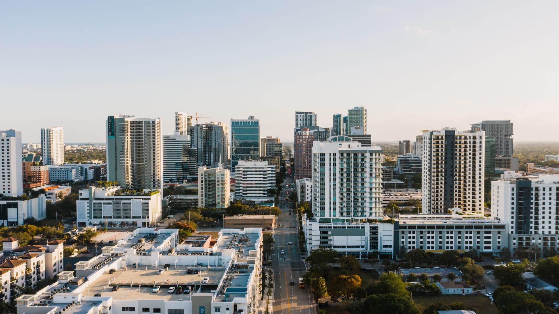 Late afternoon view across downtown Fort Lauderdale from above, residential and office towers along a straight avenue with a yellow tower crane on a building under construction