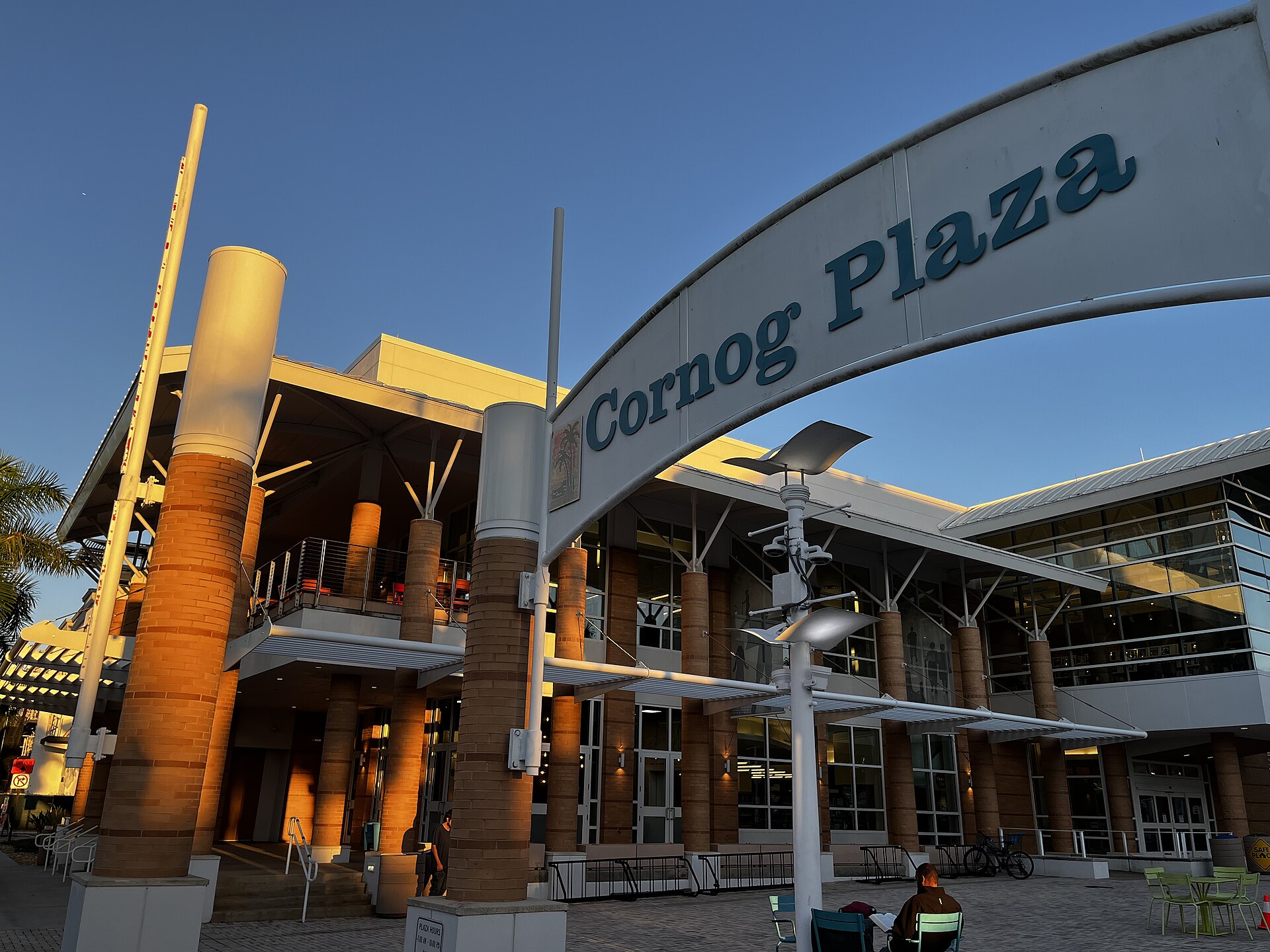 The Cornog Plaza entrance arch at the Fort Myers Regional Library, brick columns and steel canopies lit gold by late afternoon sun