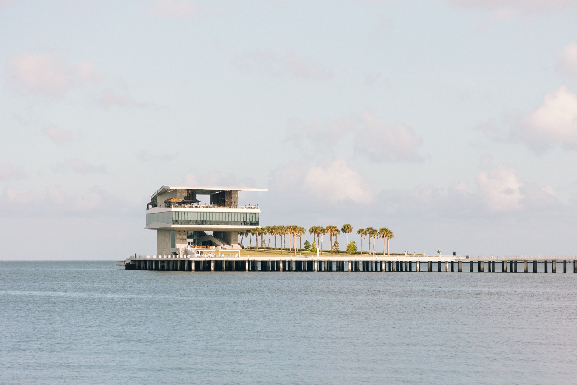 The St. Pete Pier reaching out into Tampa Bay in St. Petersburg, its cantilevered glass pier head and a row of palms along the deck seen from the water