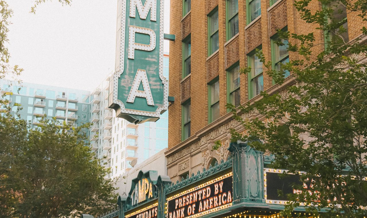 The vertical TAMPA marquee of the Tampa Theatre beside a new downtown residential tower, the market FinTruction keeps contractor books for