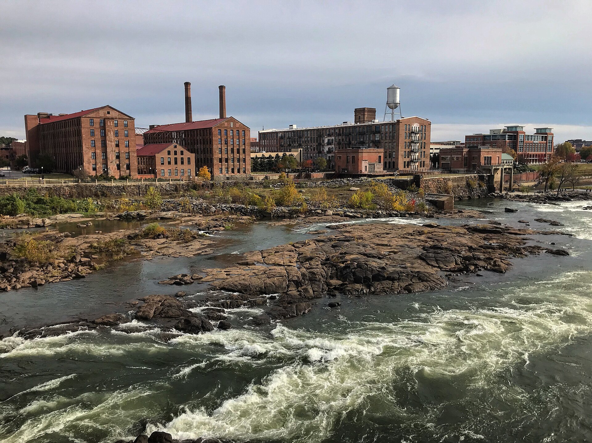 The Chattahoochee River running over rock shoals below the converted red brick Eagle and Phenix mills, smokestacks and a water tower on the Columbus, Georgia riverfront