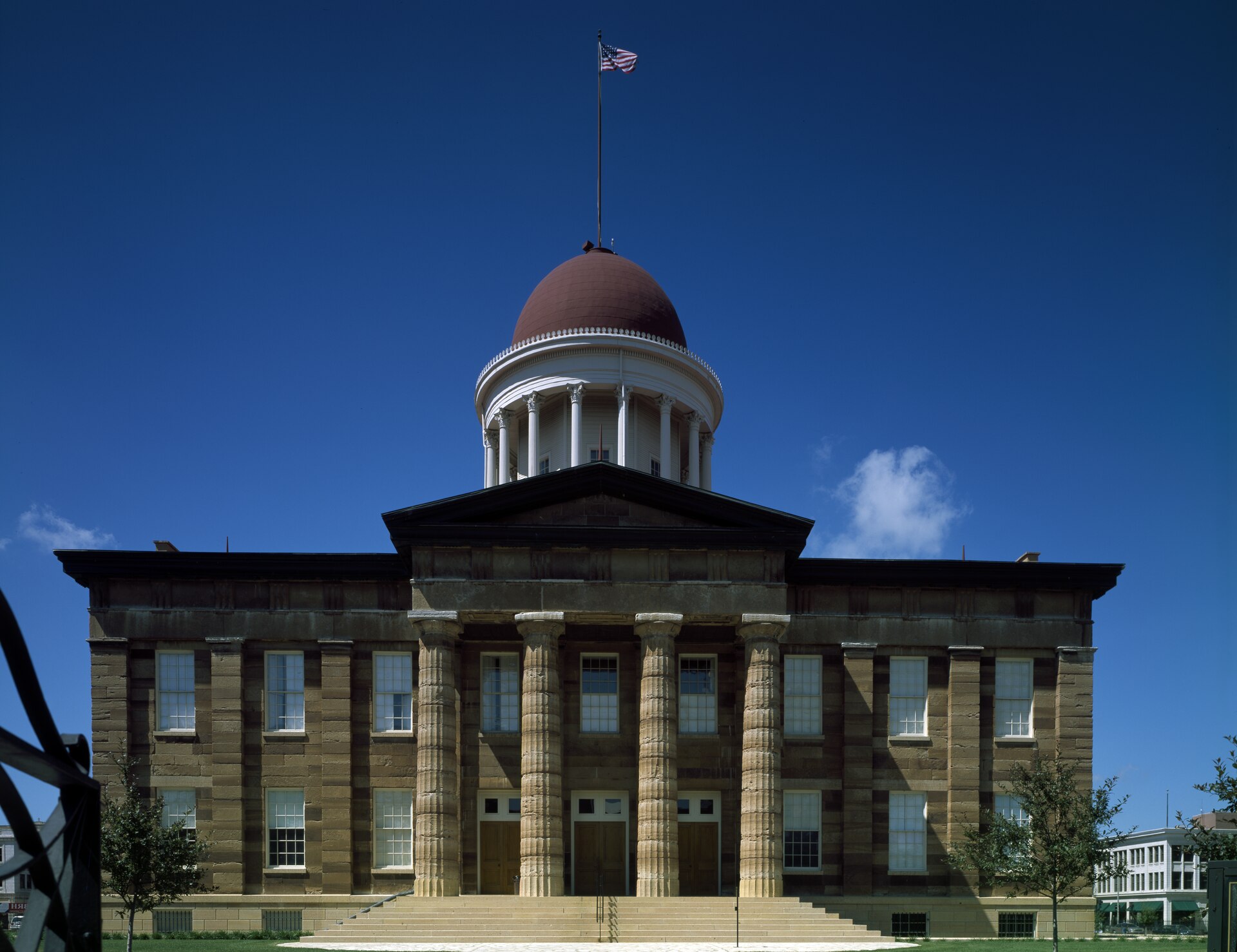 The Old State Capitol in Springfield, Illinois seen head on, a Greek Revival sandstone building with a red dome and white colonnaded cupola above the plaza steps