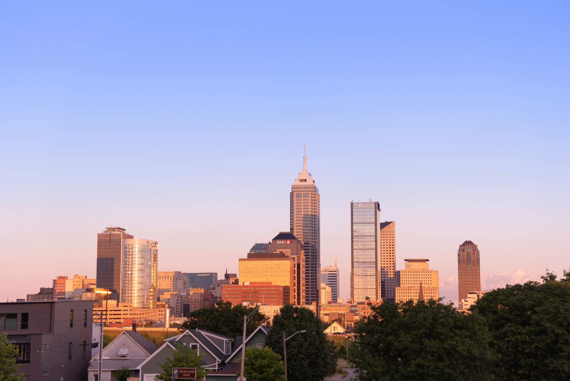 Early sunlight on the downtown Indianapolis towers seen across the rooftops and trees of a residential street below, the Indiana market FinTruction serves with construction accounting for contractors