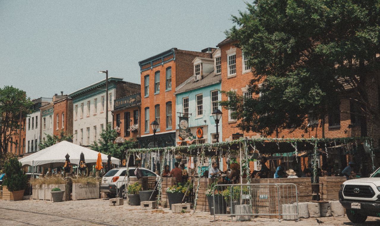 Brick and painted rowhouse storefronts with cafe seating on a cobblestone Baltimore street, the renovation market we keep books for