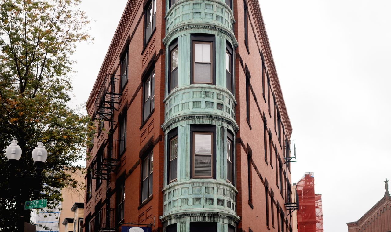 A copper-bayed brick building on Cambridge's Bow Street next to a scaffolded facade, the tight urban jobsites FinTruction job costs