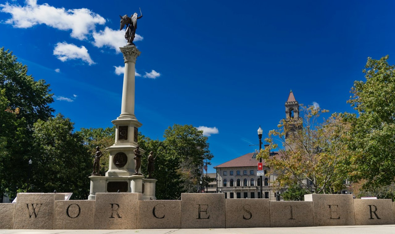Granite letters spelling WORCESTER before the war memorial and soldier statues on the Common, the Central Massachusetts market FinTruction serves