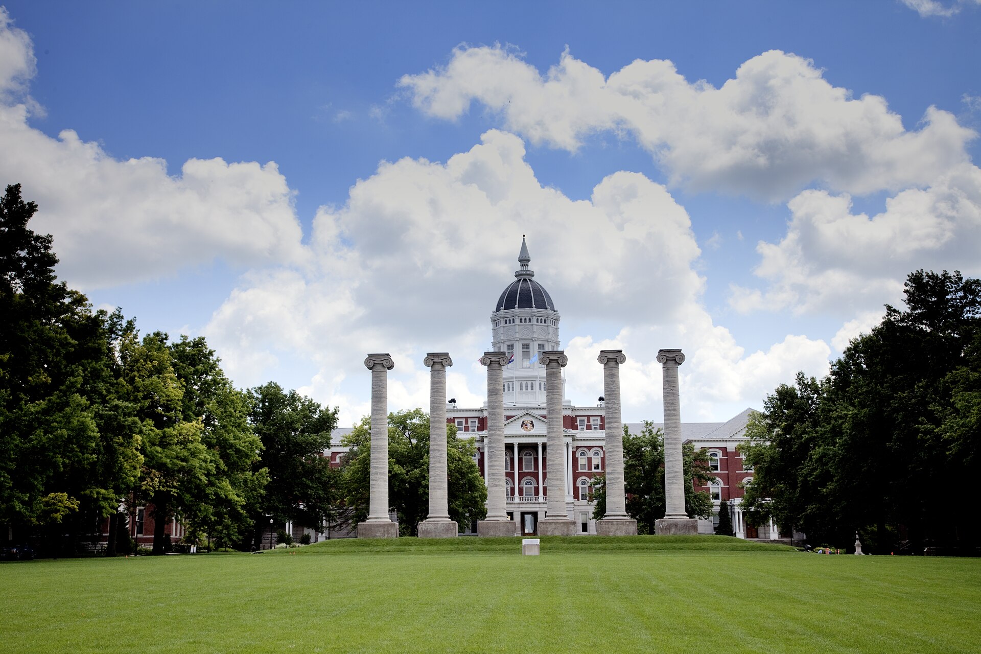The six stone Columns on Francis Quadrangle at the University of Missouri in Columbia, domed red brick Jesse Hall standing behind them under summer clouds