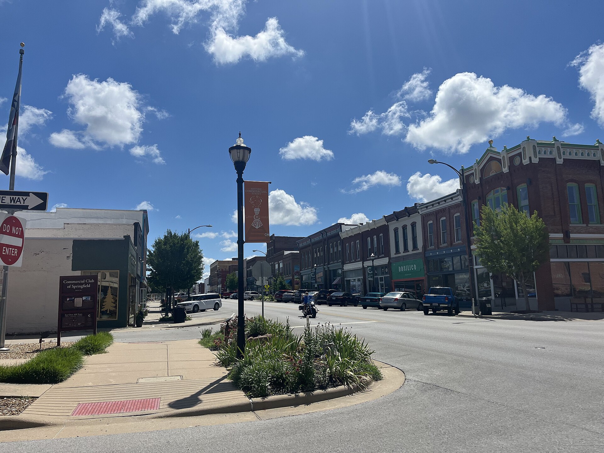 The corner of the historic Commercial Street district in Springfield, Missouri under a blue sky, restored brick storefronts along the block and a Historic Commercial Street banner on the lamp post
