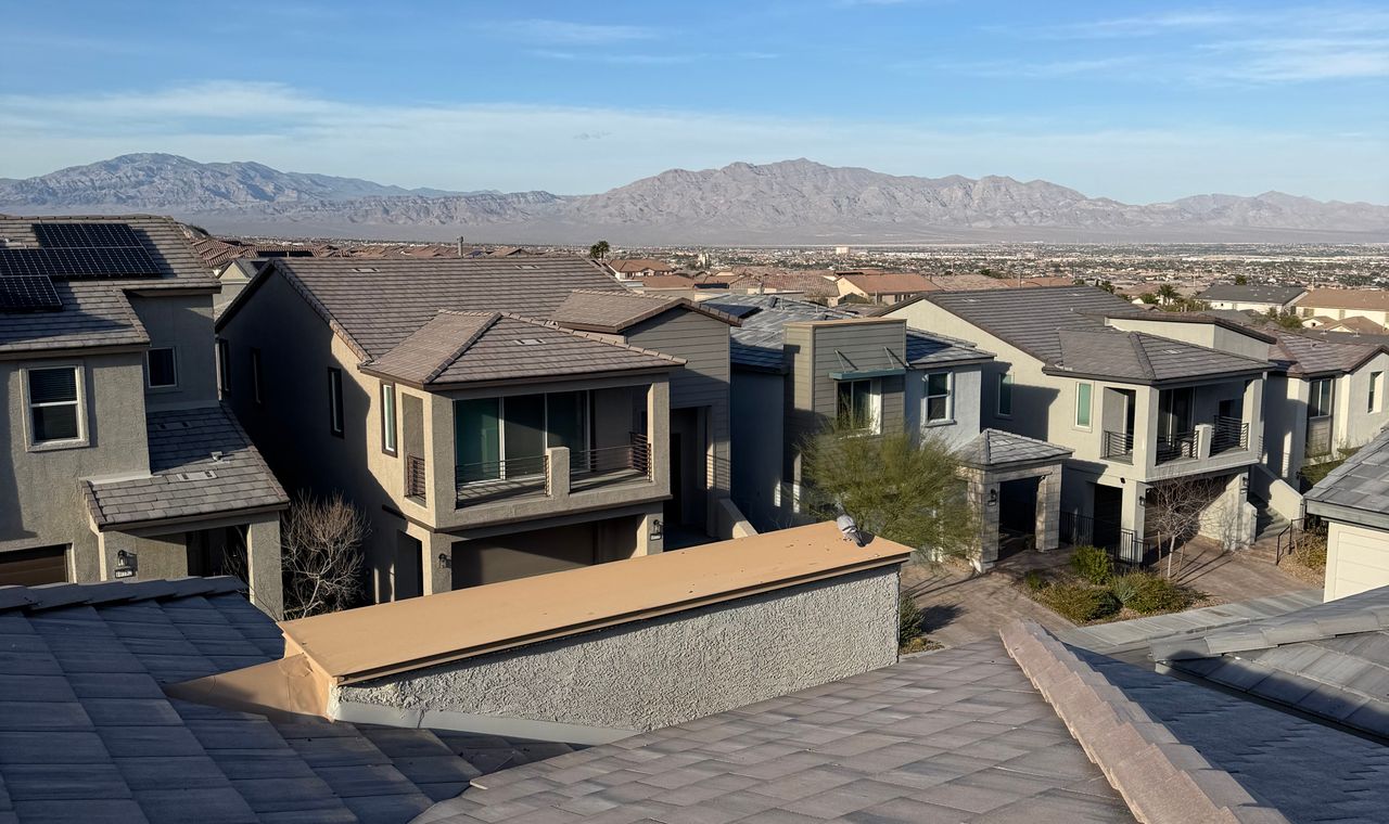 Tile-roofed two-storey homes stepping down a hillside toward the desert valley and mountains, the Henderson production housing market FinTruction supports with per-lot job costing