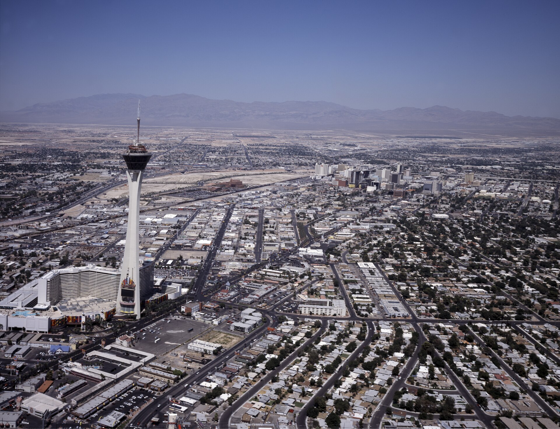 Aerial view over Las Vegas with the Stratosphere tower in the foreground, the downtown skyline beyond and desert mountains on the horizon