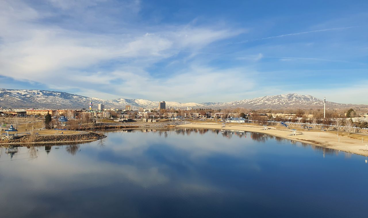 The Reno skyline reflected in a calm lake with snow-covered Sierra Nevada peaks behind, the Northern Nevada market we support with job costing