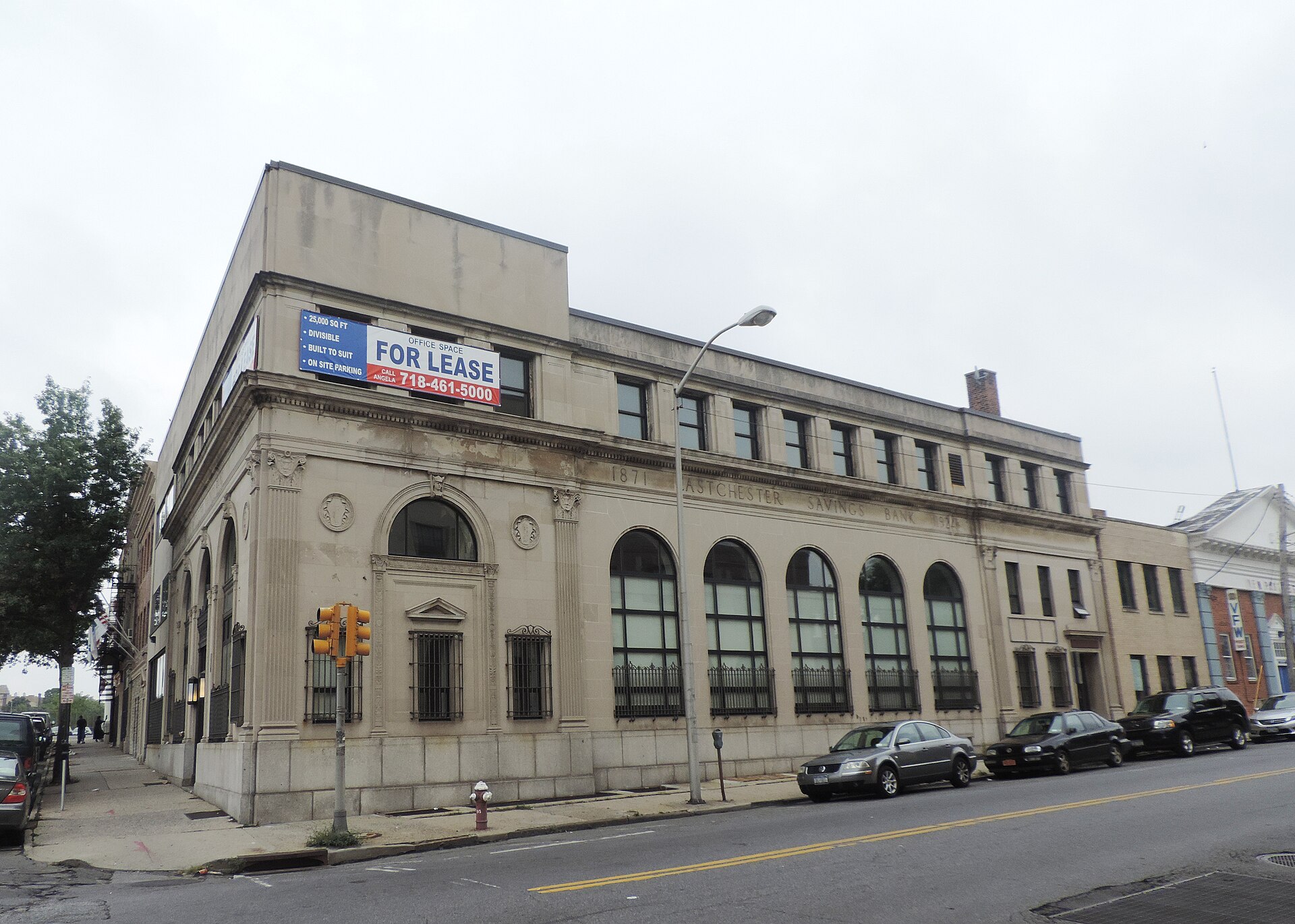 The former Eastchester Savings Bank on East First Street in Mount Vernon, a stone corner building with arched windows and a for lease banner overhead