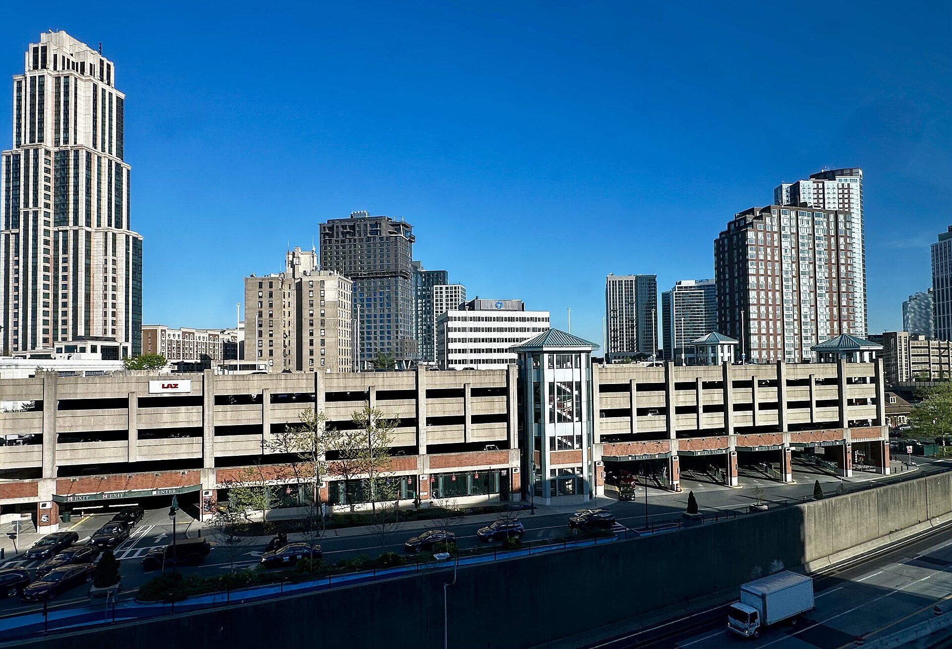 Residential towers behind the commuter parking deck and rail cut at New Rochelle station, with older brick apartment blocks between them