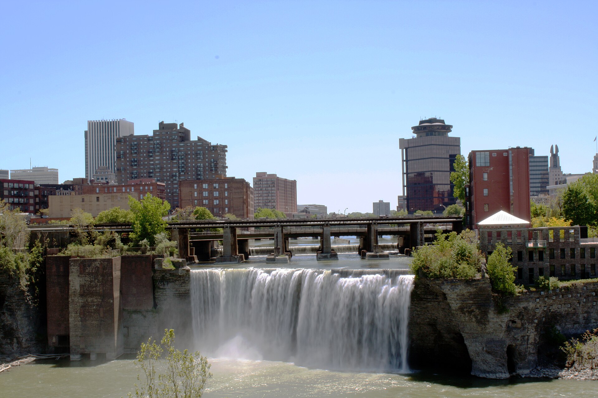 High Falls on the Genesee River in the middle of downtown Rochester, old mill buildings and a truss footbridge above the drop with the city skyline behind