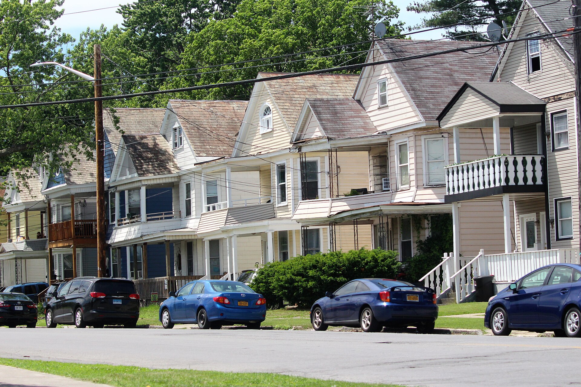 A row of two storey wood frame houses with porches, dormers and vinyl siding on McClellan Street in Schenectady, cars parked along the curb