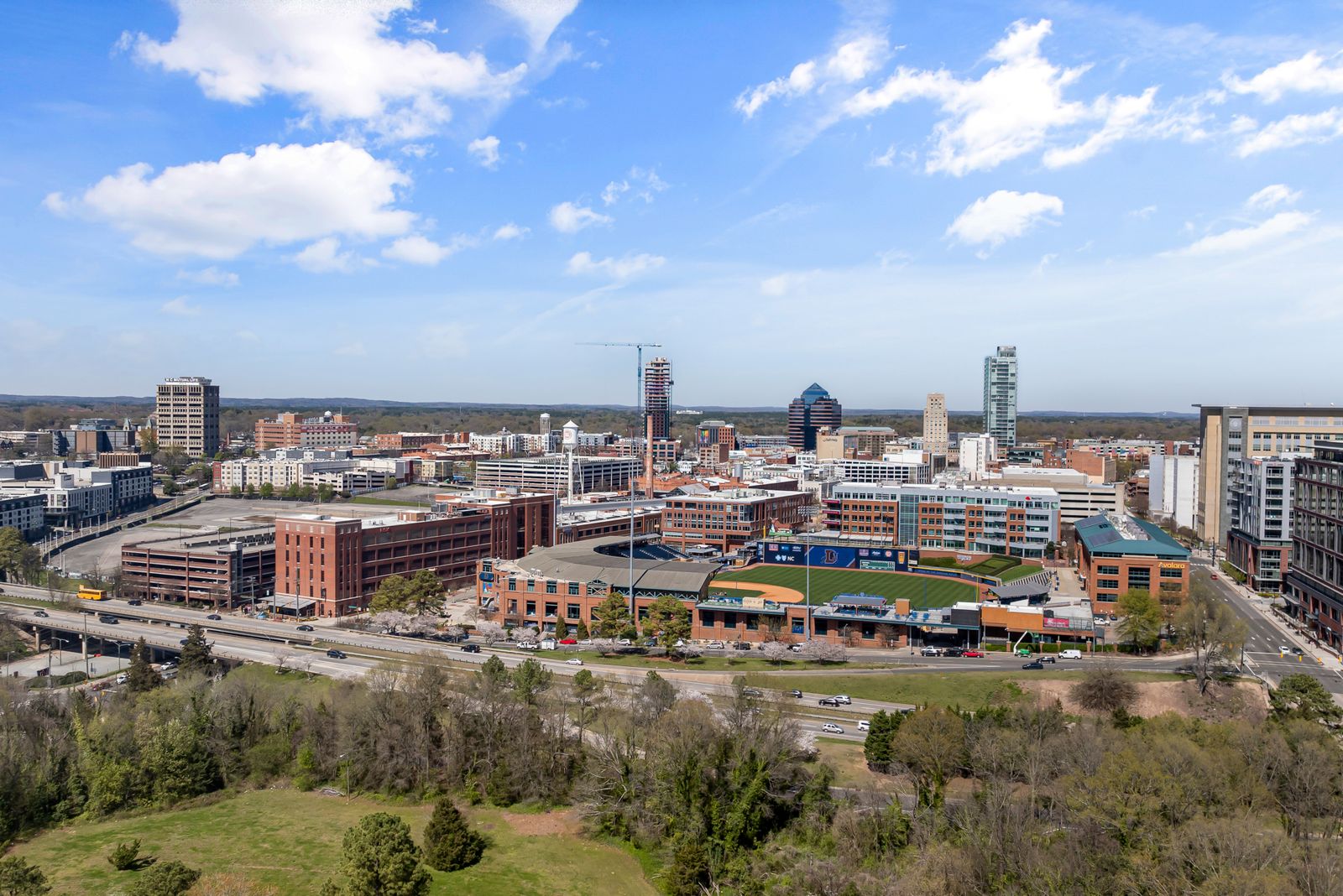 The downtown Durham skyline from the air with the Durham Bulls Athletic Park in the foreground and a tower crane over a high-rise under construction