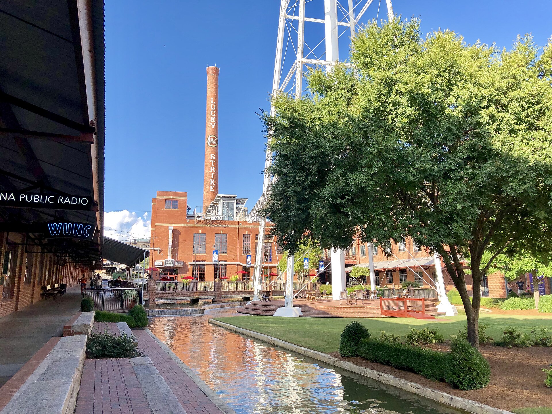 The Lucky Strike smokestack and water tower above the red brick warehouses and water channel of the American Tobacco Campus in Durham