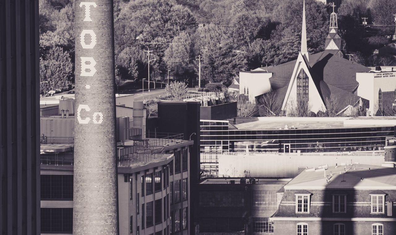 Brick smokestack lettered TOB. Co. above old factory buildings in downtown Winston-Salem, the district contractors now rebuild