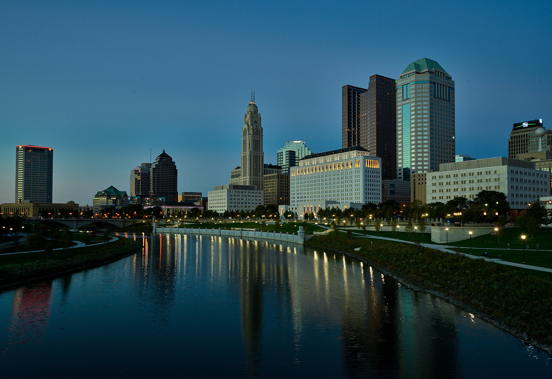 Columbus skyline at blue hour reflected in the Scioto River, LeVeque Tower lit above the lawns and lamps of the Scioto Mile