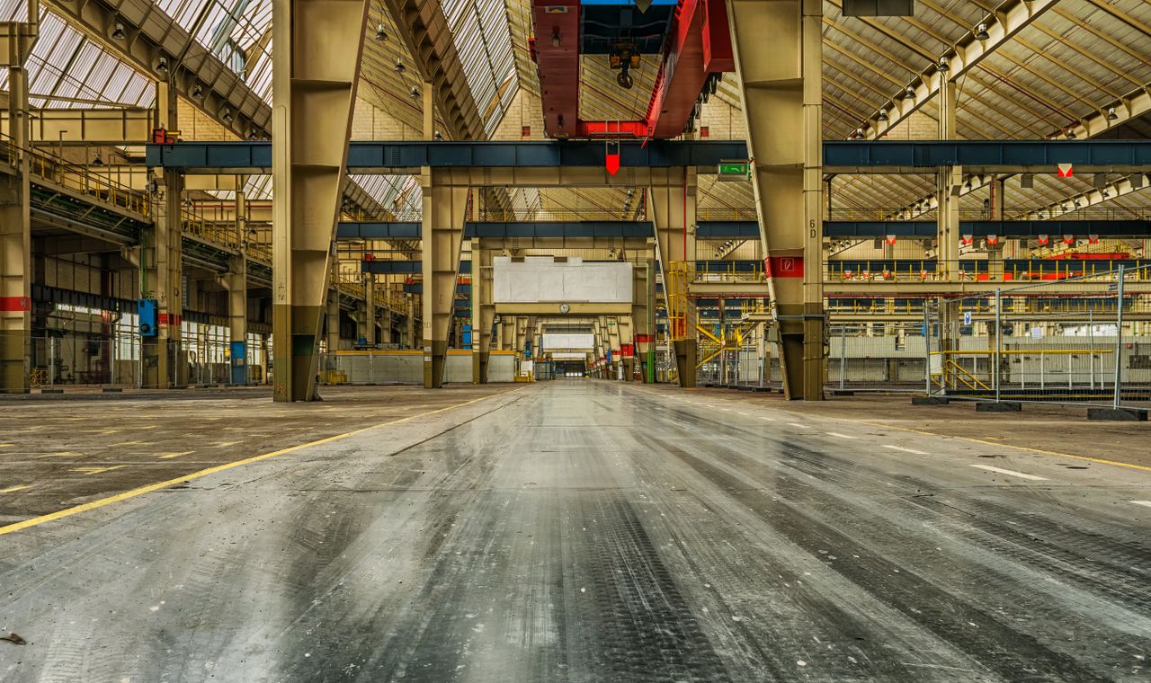 Empty plant floor with a red overhead traveling crane and steel columns, the industrial retooling work Toledo contractors cost by shutdown window