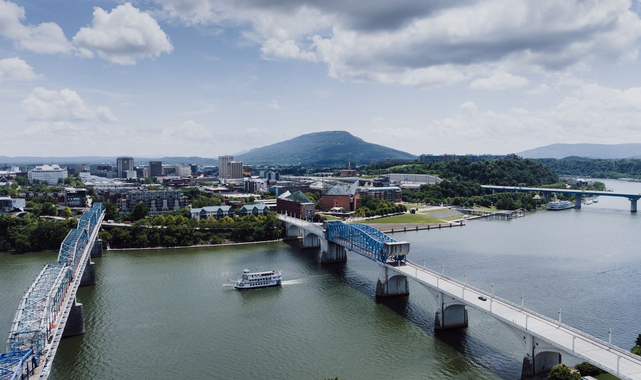 Blue truss bridges over the Tennessee River with a riverboat mid-channel and the downtown Chattanooga riverfront, the market FinTruction serves with construction bookkeeping