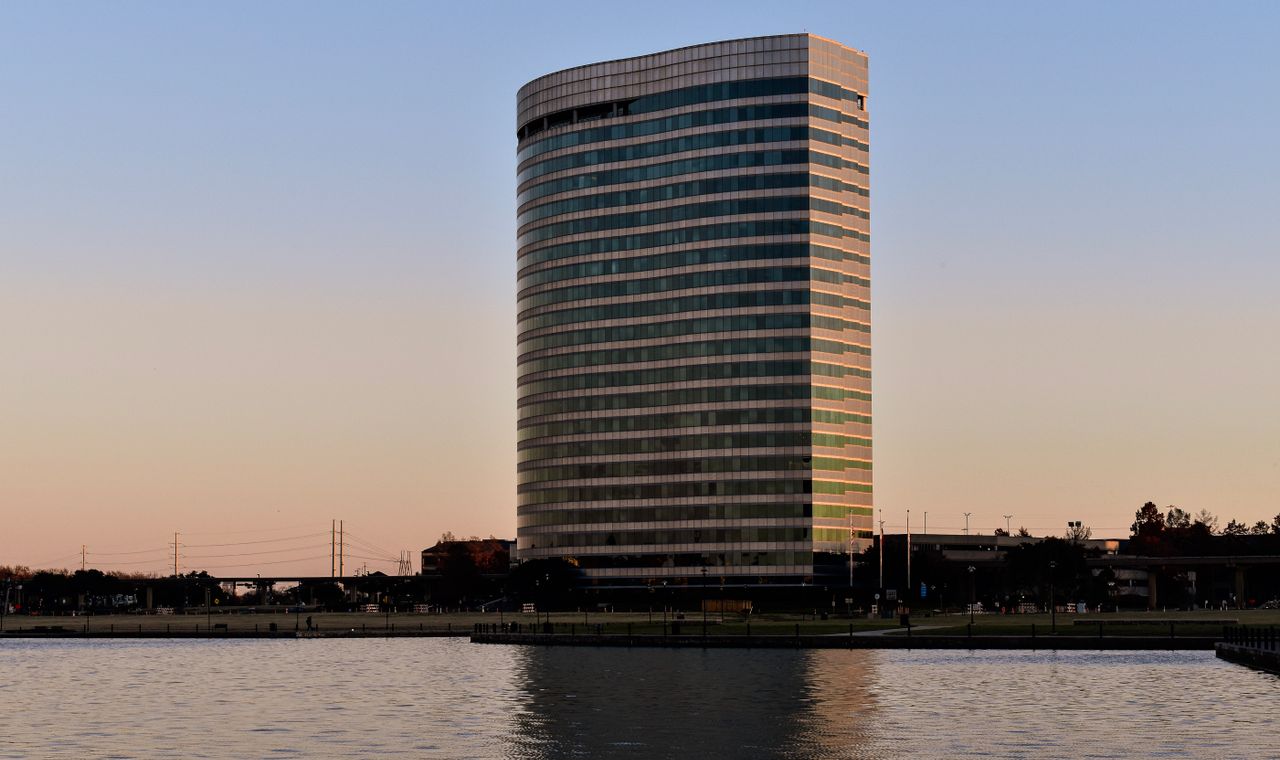 A curved glass office tower catching the sunset above Lake Carolyn in Las Colinas, Irving, where FinTruction handles job costing and WIP reporting