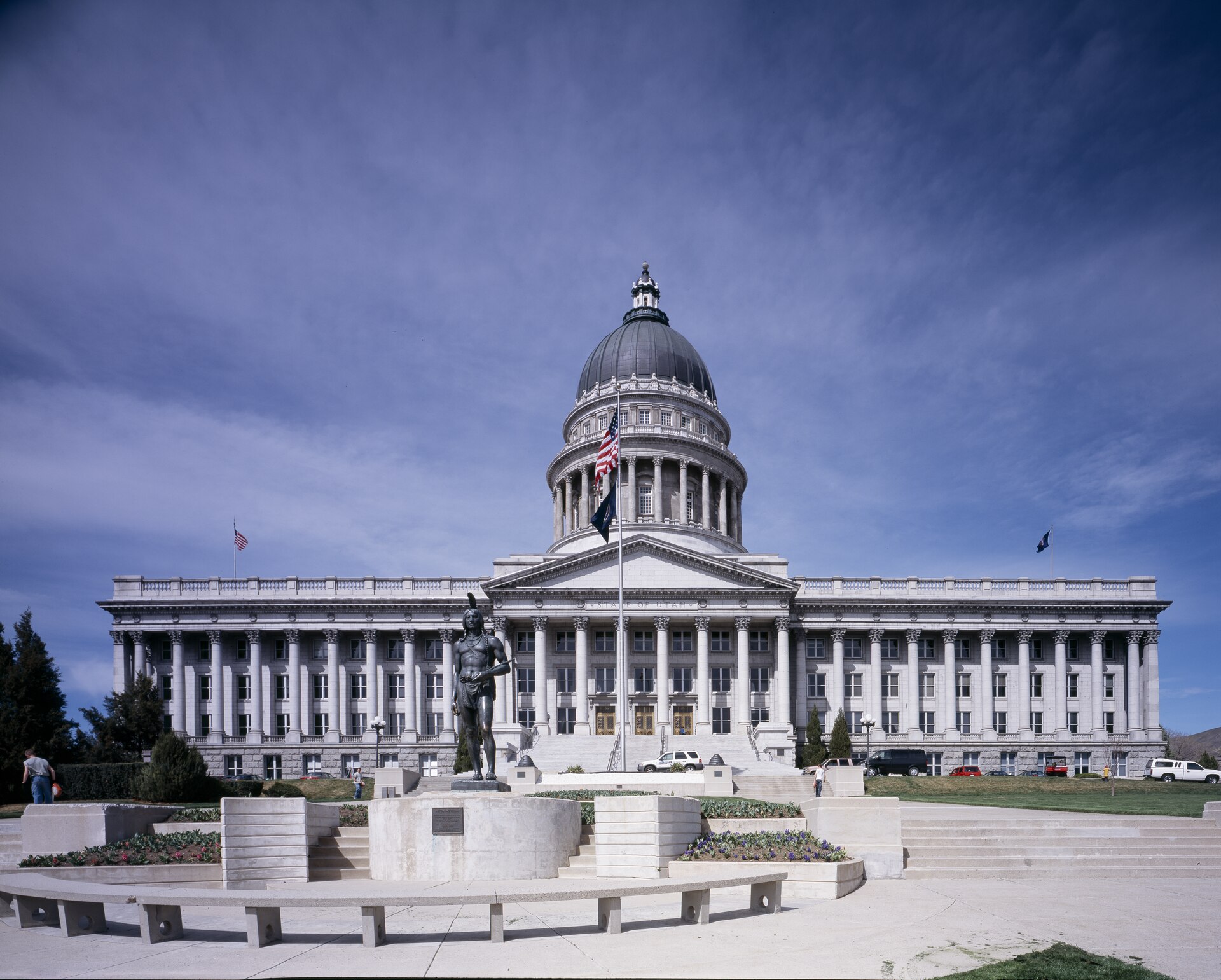 The Utah State Capitol in Salt Lake City, a granite dome and long colonnade above terraced steps with flags and a bronze statue in front