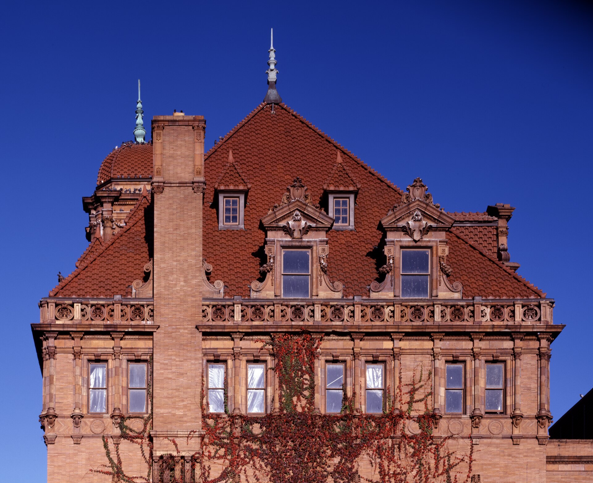 Red clay tile roof and carved stone dormers of Richmond Main Street Station against a deep blue sky, Virginia creeper climbing the brick below
