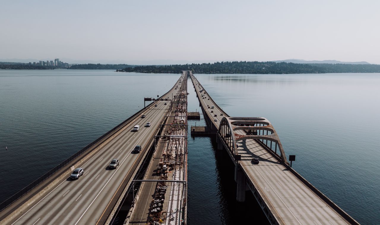Traffic on the twin floating bridges across Lake Washington with light rail track work in the center lanes and the Bellevue skyline on the horizon