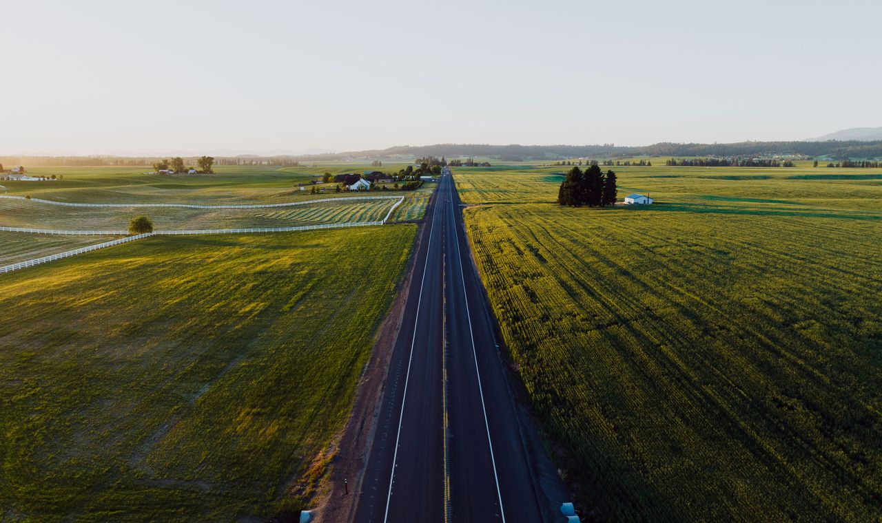 A two-lane highway running straight through farm fields at sunrise outside Spokane, the rural catchment contractors here travel to reach