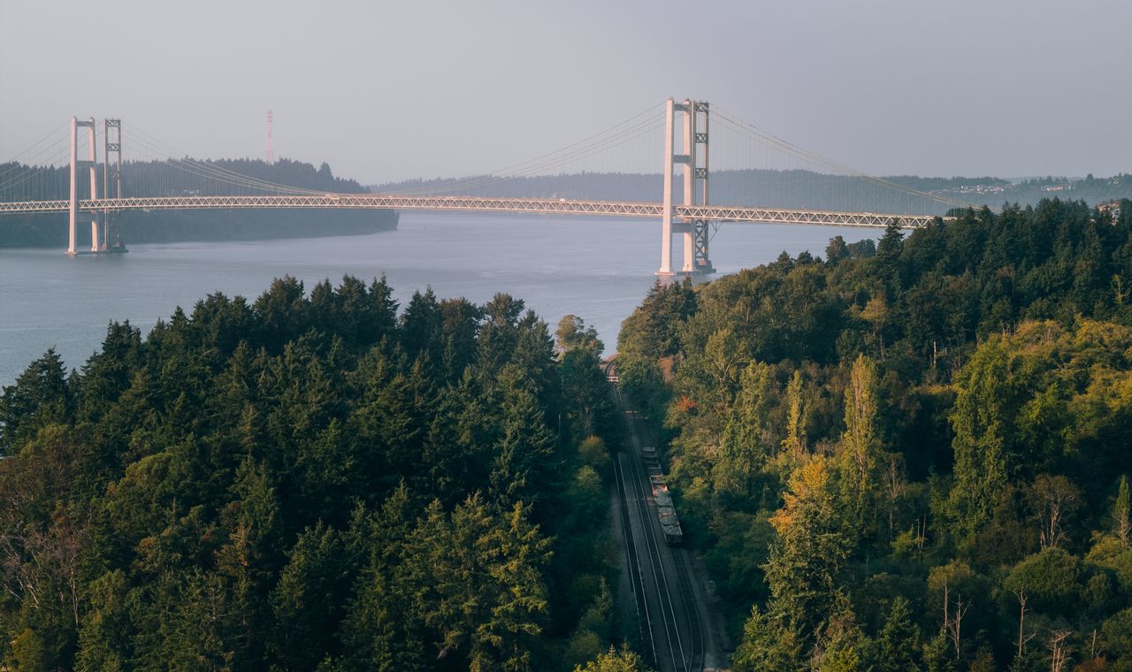 The Tacoma Narrows Bridge above evergreen forest and a rail line along the water, part of the Pierce County market we keep contractor books for